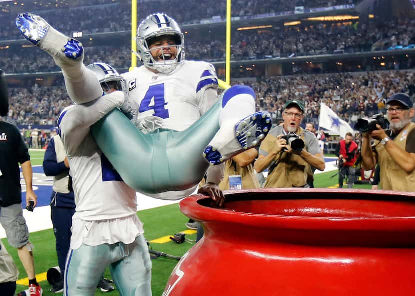Dallas Cowboys running back Ezekiel Elliott (21) throws quarterback Dak Prescott (4) into...