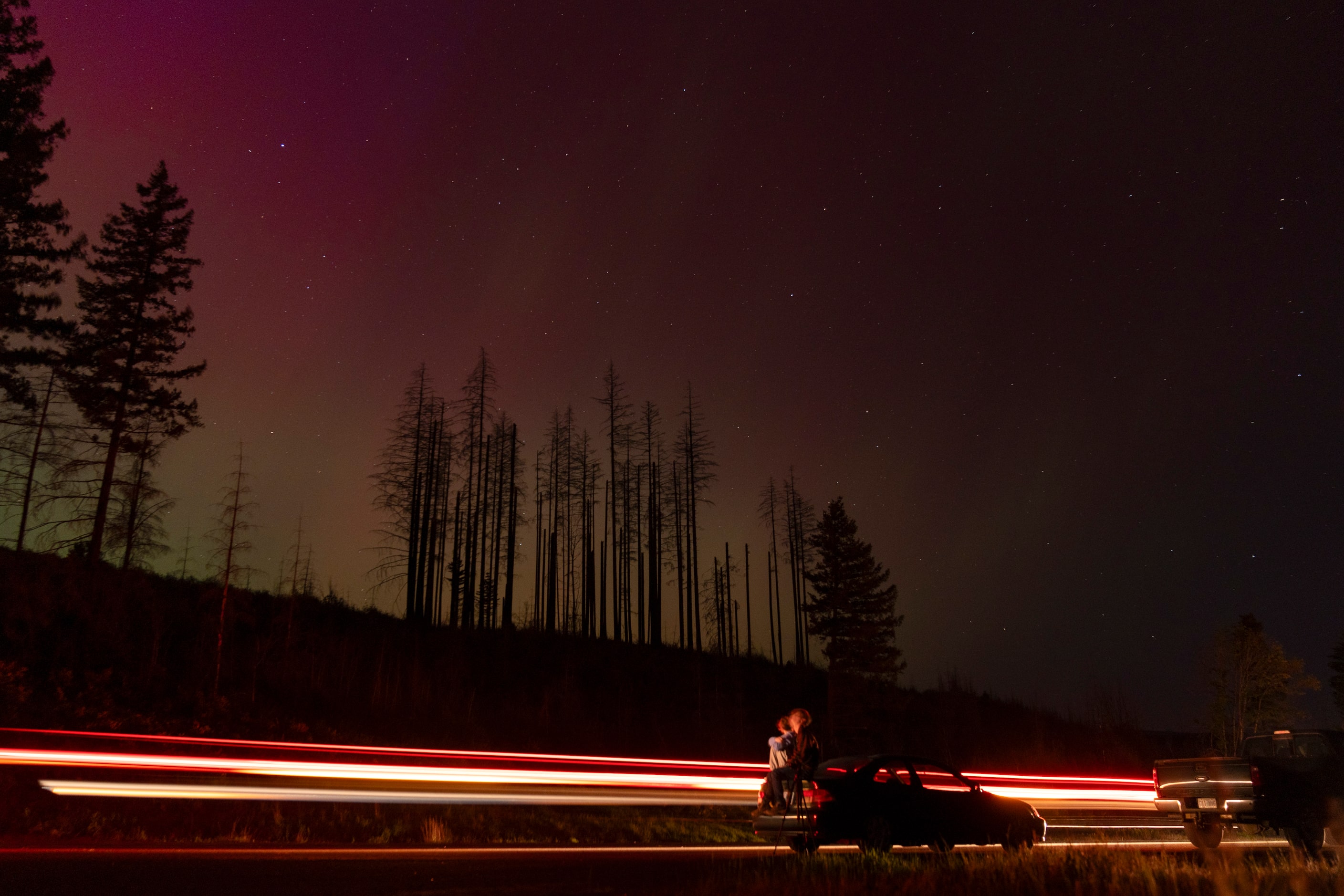 In this image taken with a long exposure, cars pass by as people look at the night sky...