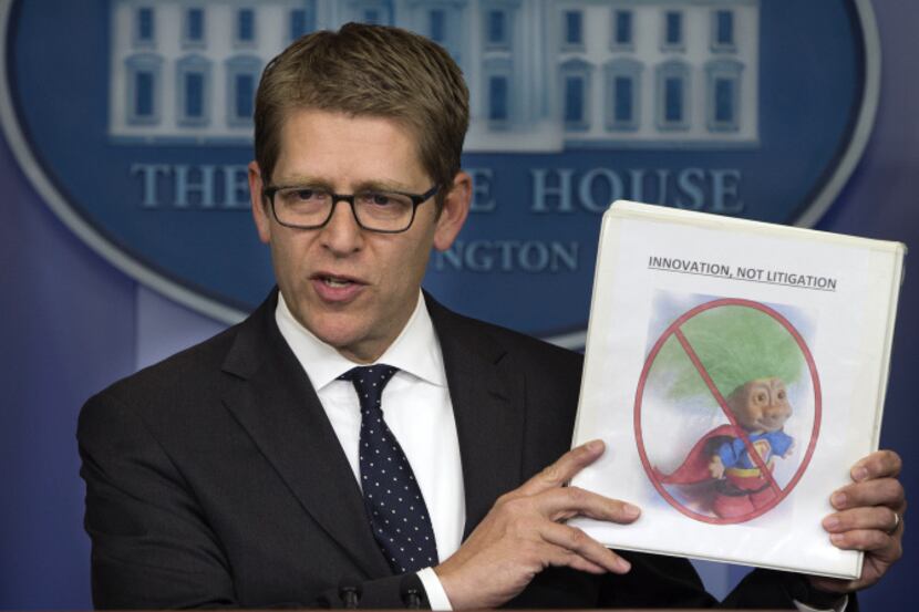 White House press secretary Jay Carney holds up a folder with an image of a troll and the...