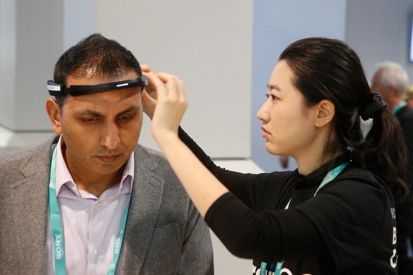 Yuwei Gu, right, of Ampligence, helps Ammad Khan with the BrainCo brainwave-sensing headband...