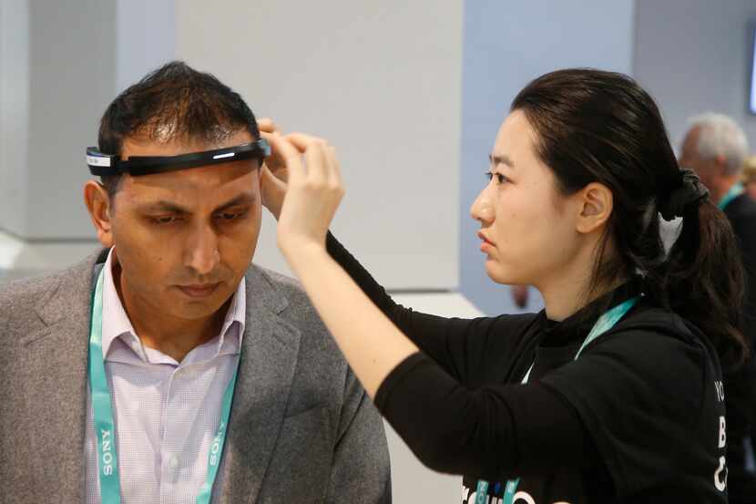 Yuwei Gu, right, of Ampligence, helps Ammad Khan with the BrainCo brainwave-sensing headband...