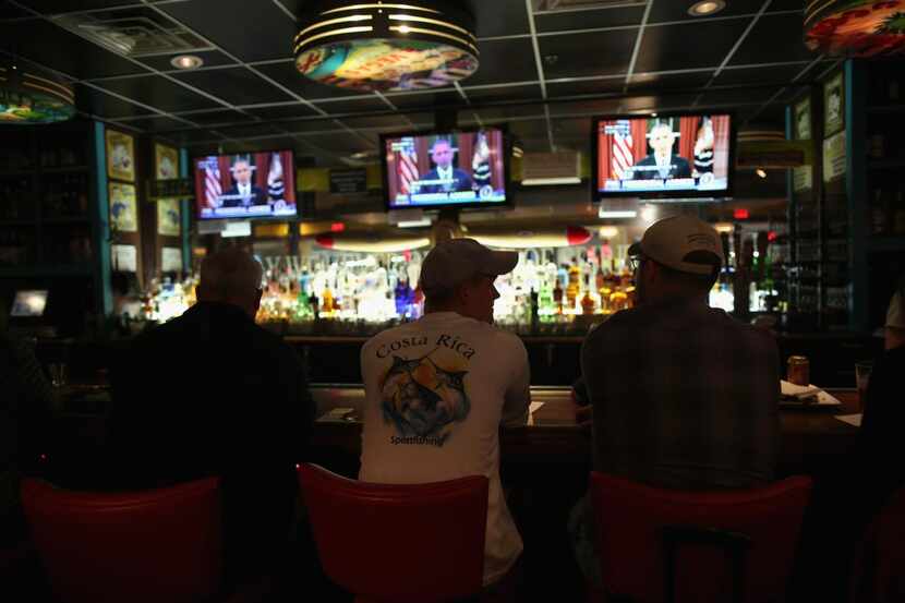 
Bar patrons at Dallas/Fort Worth International Airport watch as President Barack Obama...