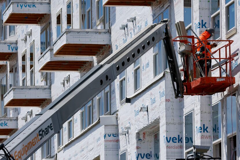 A construction worker uses a lift to work on the exterior of The Alexan Apartments along...