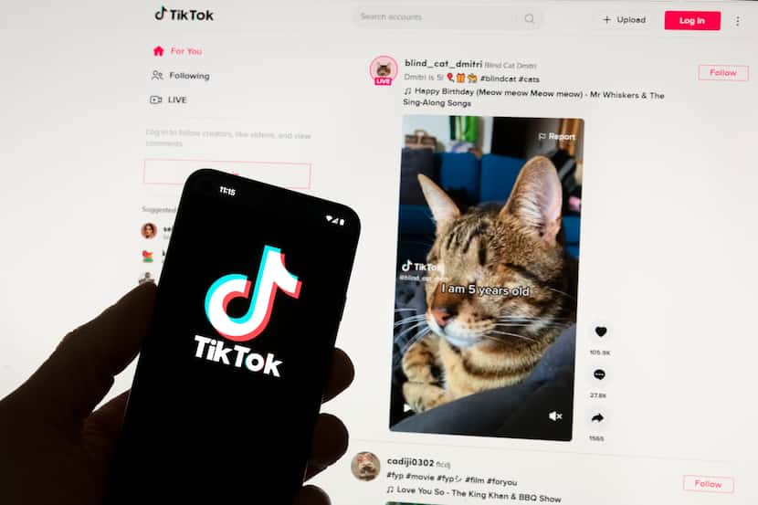 The TikTok logo is seen on a mobile phone in front of a computer screen that displays the...