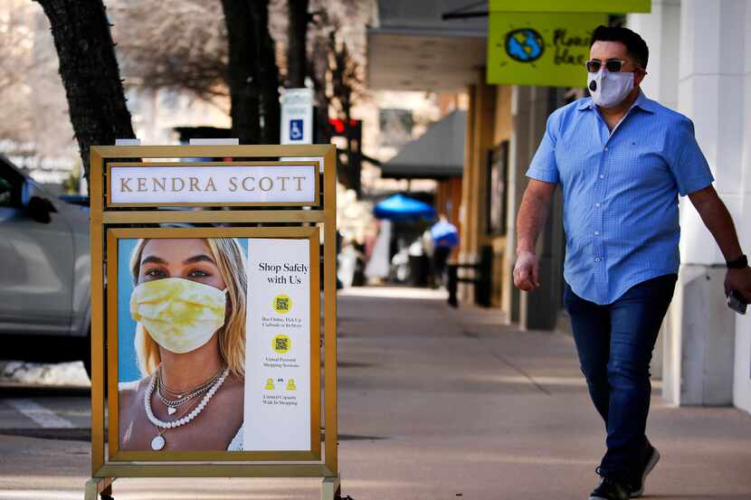 A man walks past a COVID practices sign outside the Kendra Scott store at the West Village...