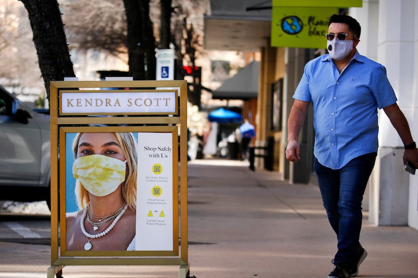 A man walks past a COVID practices sign outside the Kendra Scott store at the West Village...