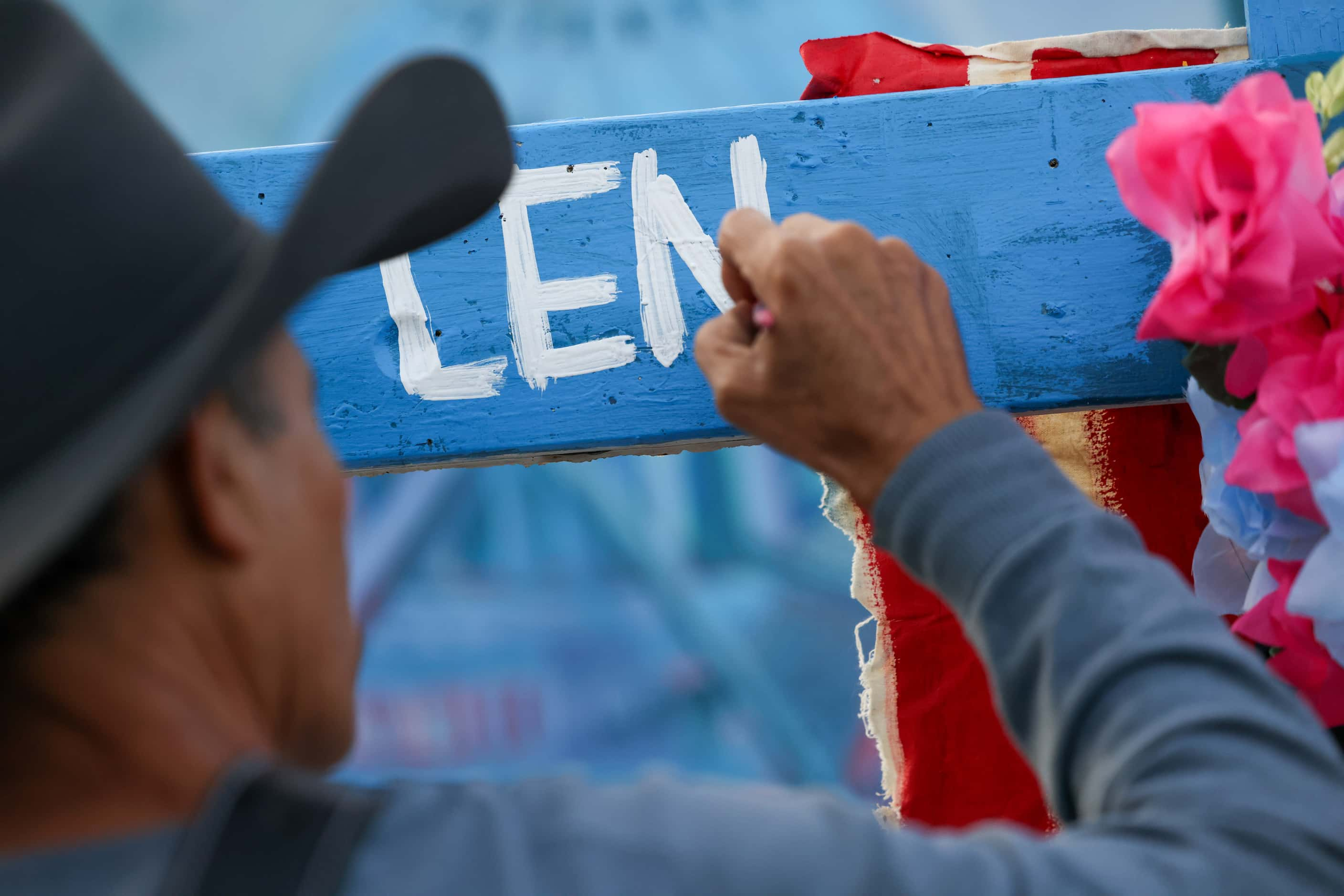 Artist Roberto Márquez paints the name of Len Root, one of three identified victims of the...