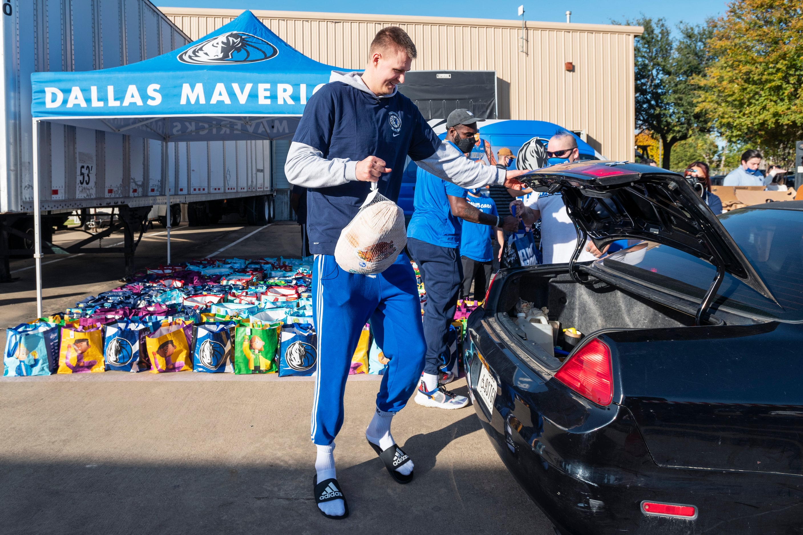 Dallas Mavericks player Kristaps Porzingis loads a frozen turkey into a car's trunk as he...