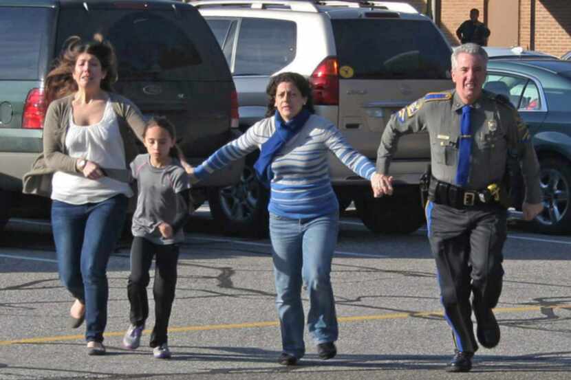 A police officer led two women and a child away from Sandy Hook Elementary School after a...