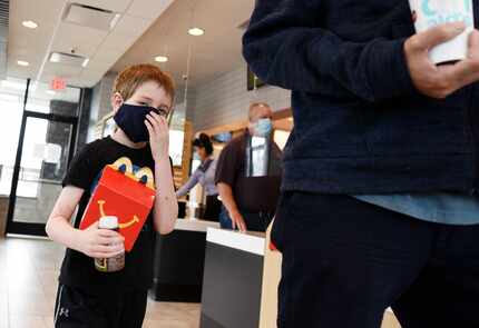 Hudson Ford, 6, adjusts his face covering after receiving his food order with his father at...