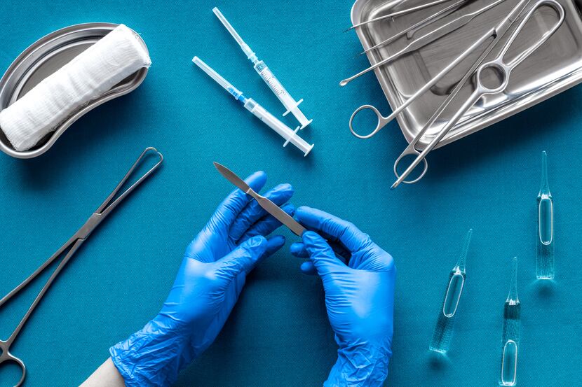 Doctor's hands takes scalpel on blue background with surgical tools.