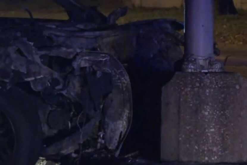 The charred remains of a car rest against a light pole after a crash that killed two people...