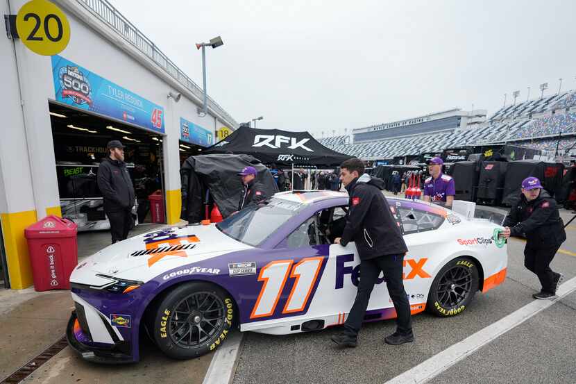 Crew members push Denny Hamlin's car to his garage after a practice session was cancelled...