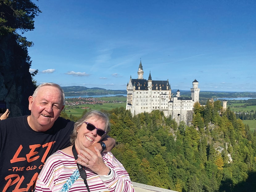 Two adults pose on a hilltop with a white castle in the background.