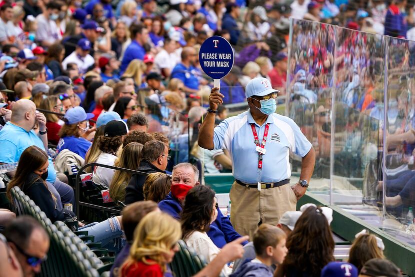 An usher holds a sign encouraging fans to wear face coverings between innings of a game...