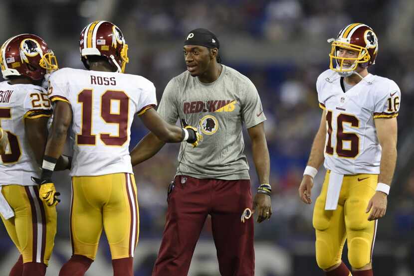 Washington Redskins quarterbacks Robert Griffin III, center, and Colt McCoy (16) greet wide...