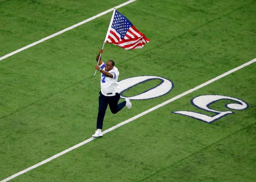 Former Dallas Cowboys player George Teague leads the team onto the field with the U.S. flag...