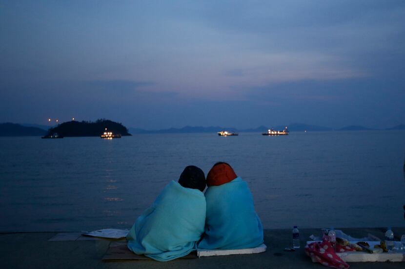 Relatives of passengers aboard the sunken ferry Sewol sit near the sea at a port in Jindo,...