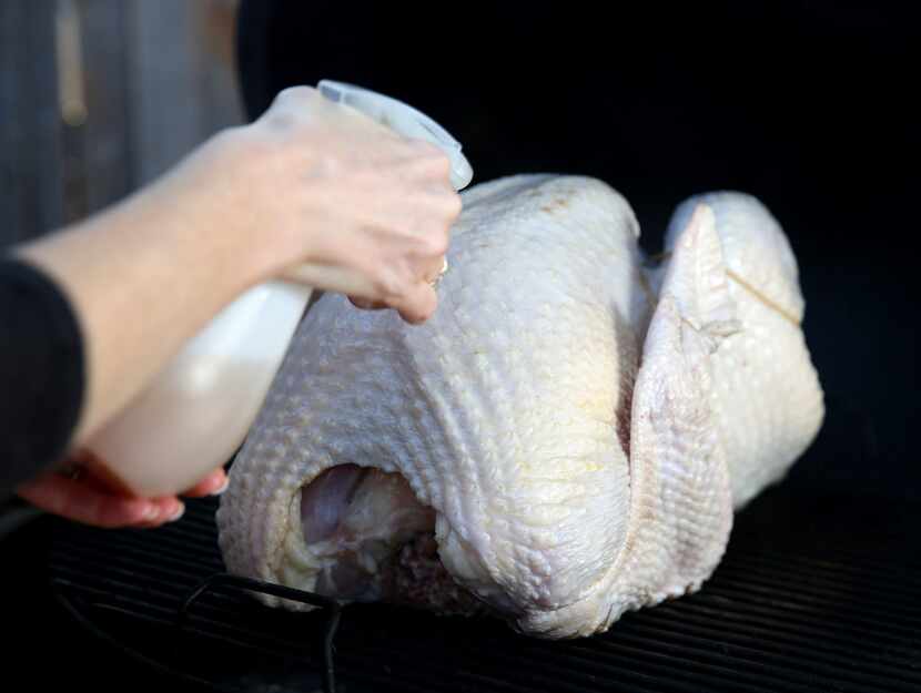 Rebecca White sprays a turkey with apple juice before it's smoked at her home in Plano.