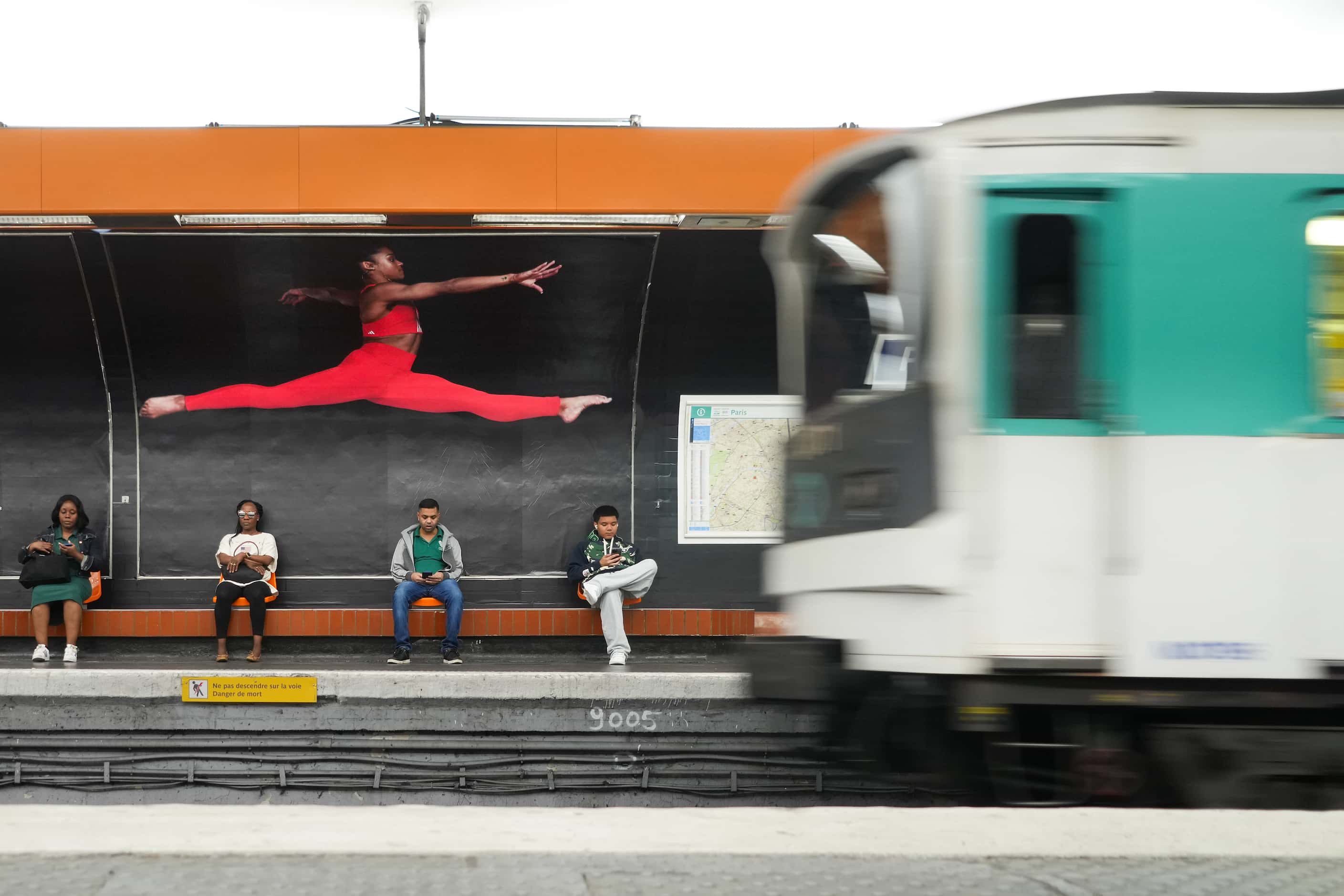 People wait for a train in a metro station under an image of French gymnast Mélanie de Jesus...