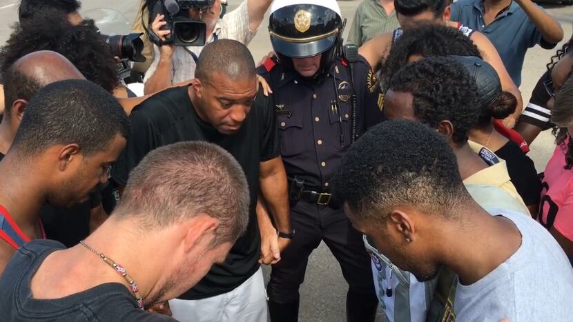 Protesters, counterprotesters and a Dallas police officer pray together at the end of a...