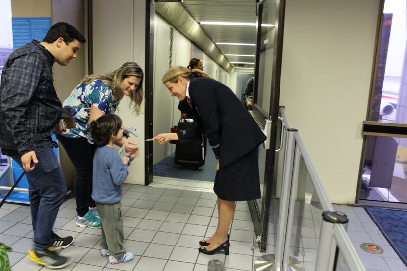 An American Airlines flight attendant gives a wings pin to a  child boarding a plane at DFW...