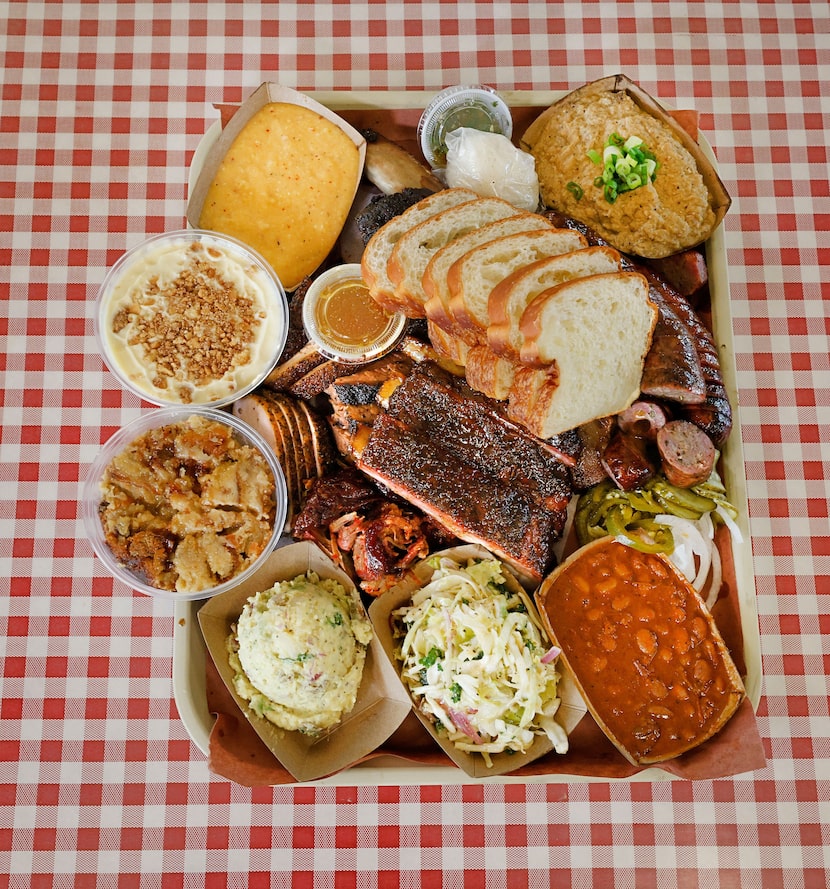 A platter with brisket, sausage, turkey, ribs, homemade brioche, sides and desserts, is seen...