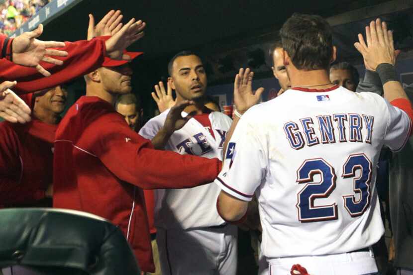 Texas center fielder Craig Gentry is greeted in the dugout by teammates after scoring in the...