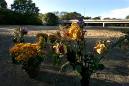  A woman walking with her dog passes a white cross and some flowers alongside the White Rock...