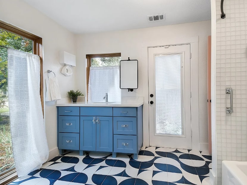 Bathroom with blue vanity, patterned floors and windows.