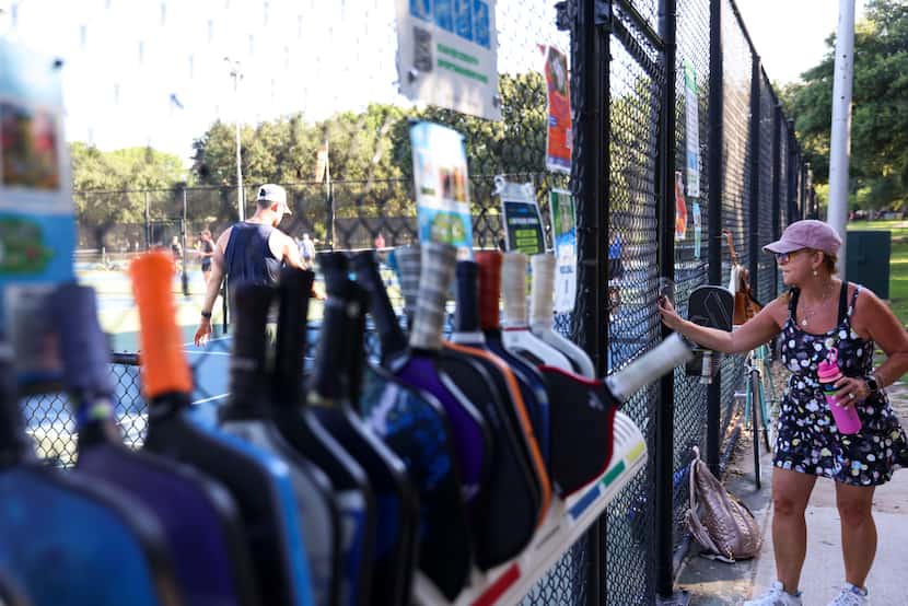 Debbie Stenzler enters the pickleball courts through a gate alongside the rack where players...