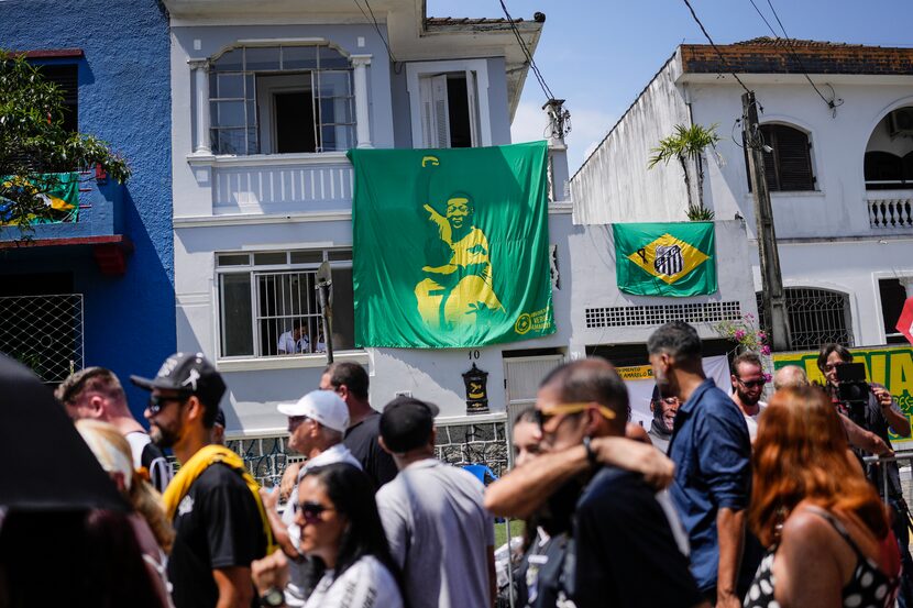 Una pancarta con la imagen de Pelé cuelga de una vivienda, detrás de la fila de gente que...