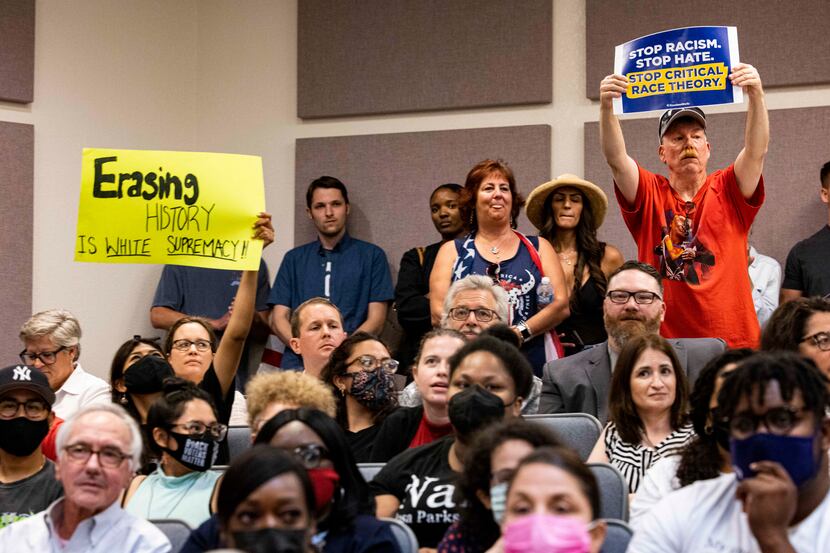 A community member holds a "Erasing history is white supremacy" sign as someone holds a...