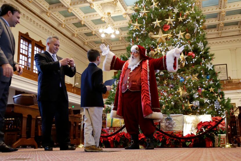 Bill French, right, dressed as Santa Claus, talks with Reagan Bohac, 8, right, son of State...
