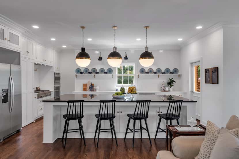 A kitchen has a large island in the center with four stools. The kitchen has stainless steel...