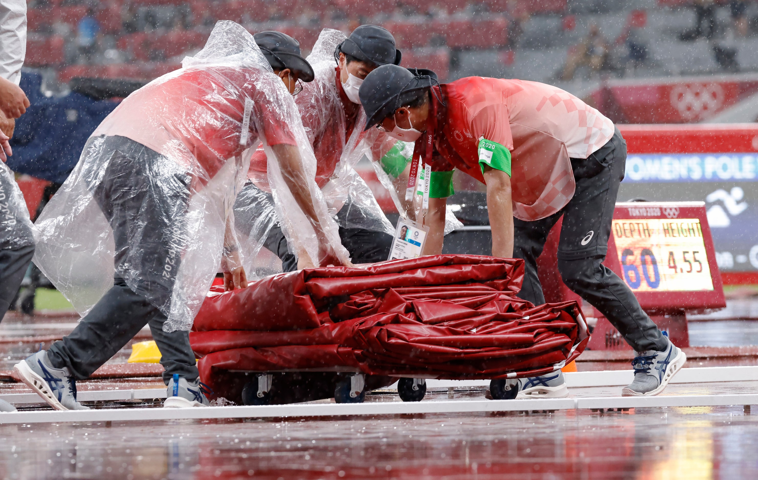 Crew for the Olympics work on getting a cover out for the mat in the pole vault area as it...