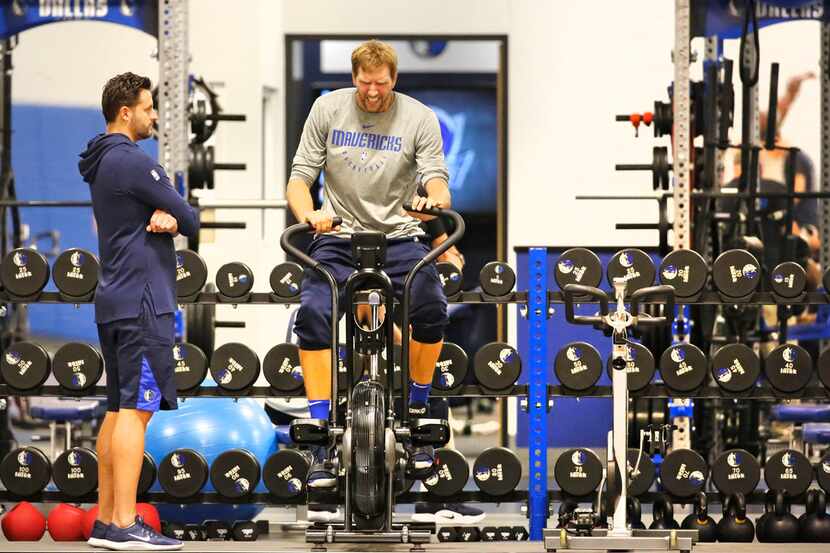 Dallas Mavericks veteran Dirk Nowitzki works out on an exercise bike under the watchful eye...