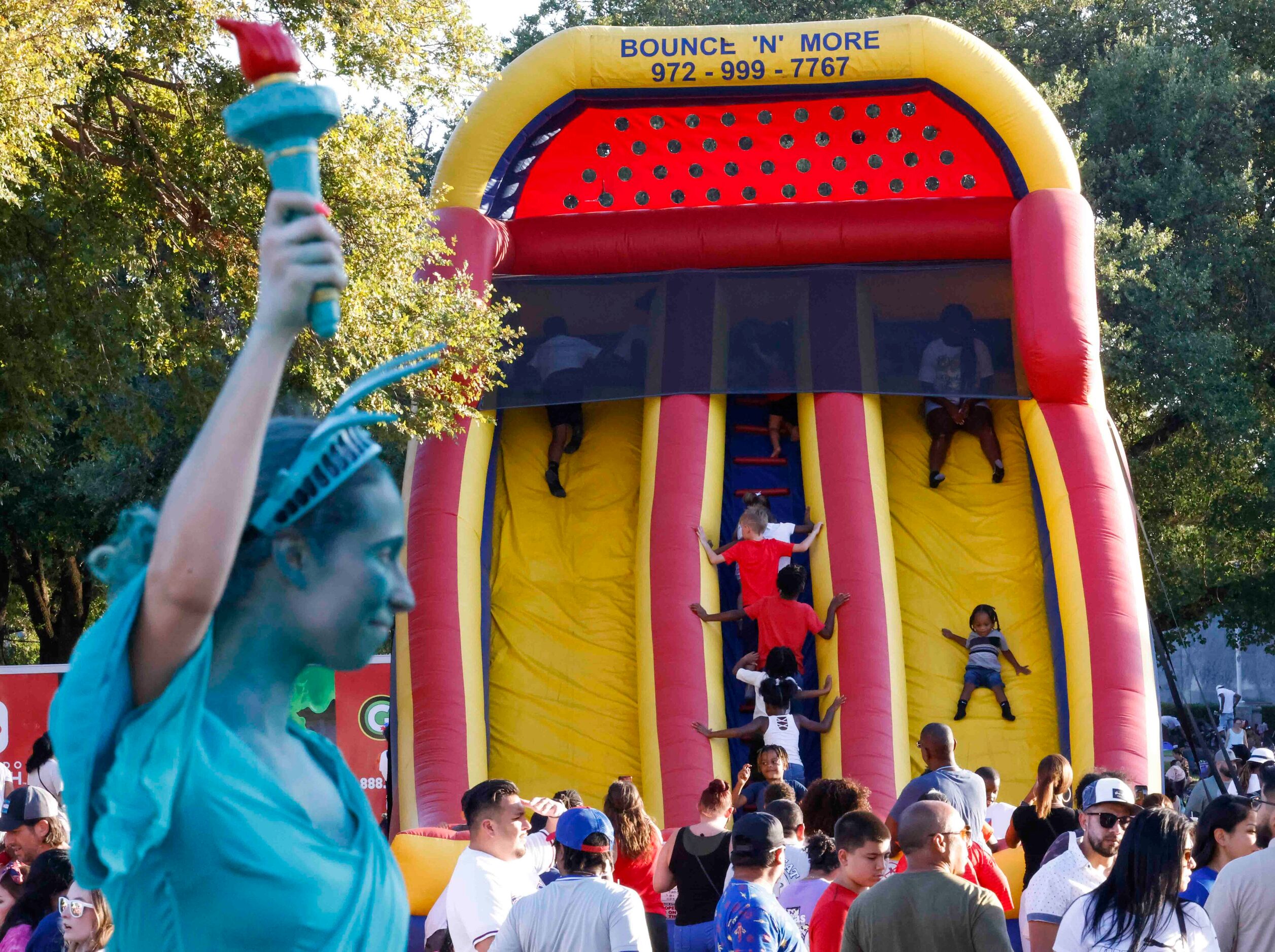 Kids enjoy their time on the slide as Anna Gliday, dressed a Statue of Liberty poses for...