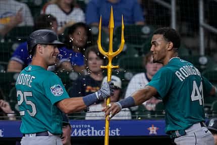 Seattle Mariners' Dylan Moore (25) is presented with a trident by Julio Rodriguez after...