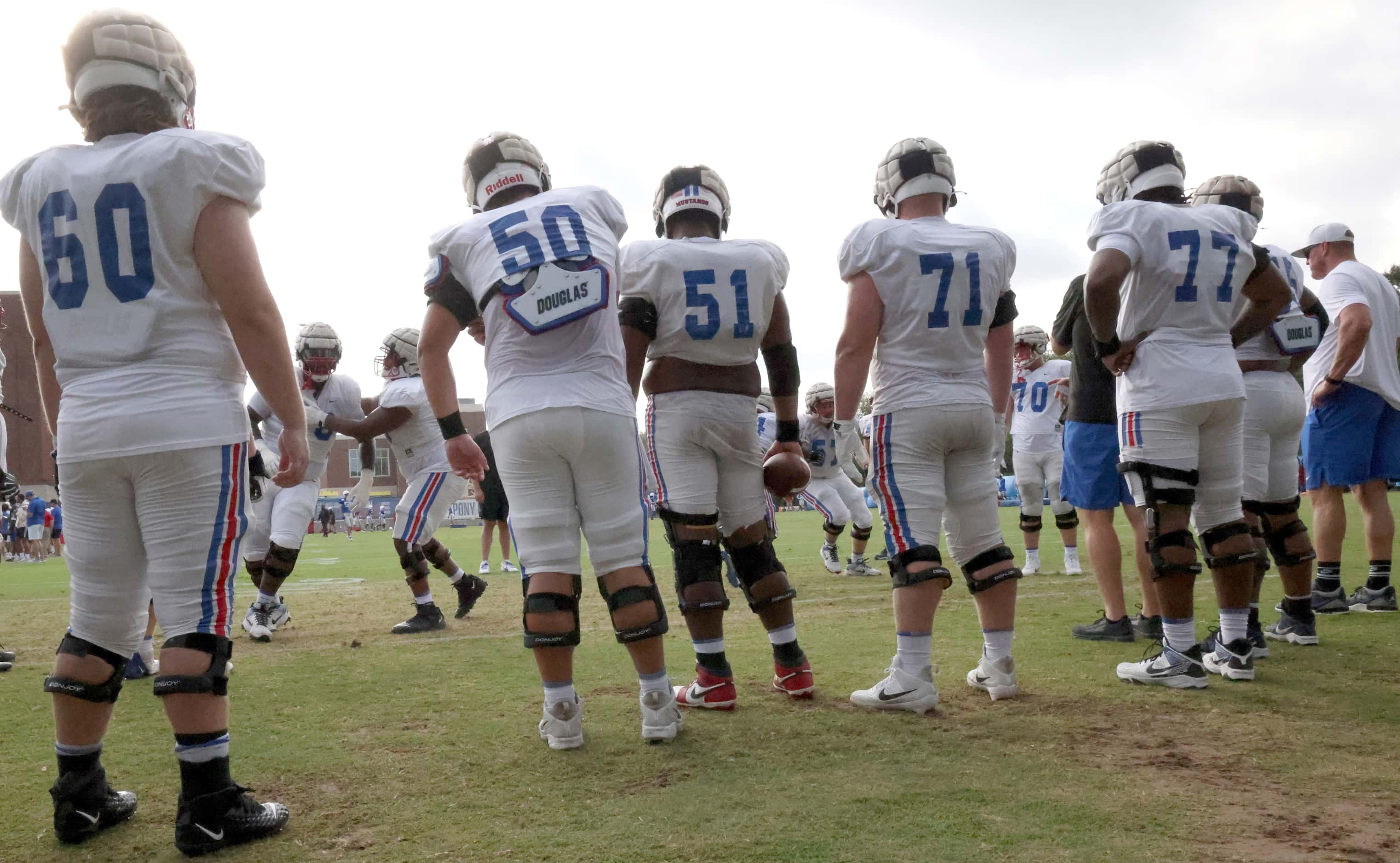 SMU offensive linemen look on as they await their turn to work on a blocking drill conducted...