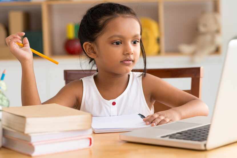 Female Indian child working on homework in front of a laptop.