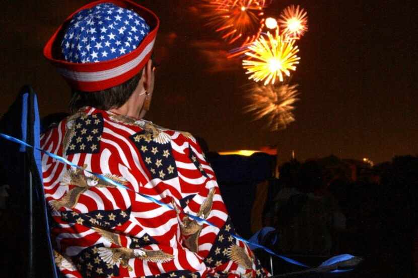 A woman in a patriotic shirt watches fireworks at Carrollton/Farmer Branch ISD athletic...