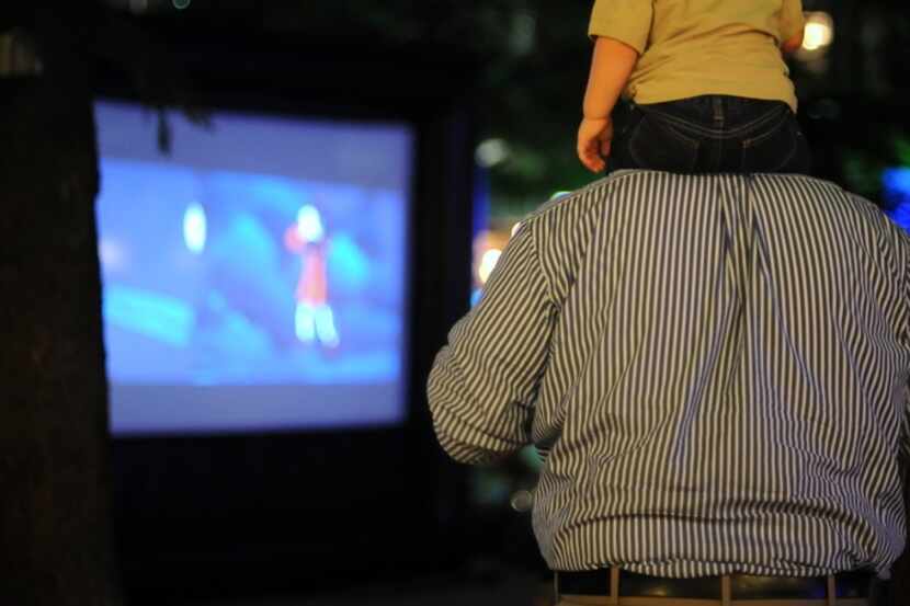A boy sits on his dad's shoulders during an outdoor movie screening.