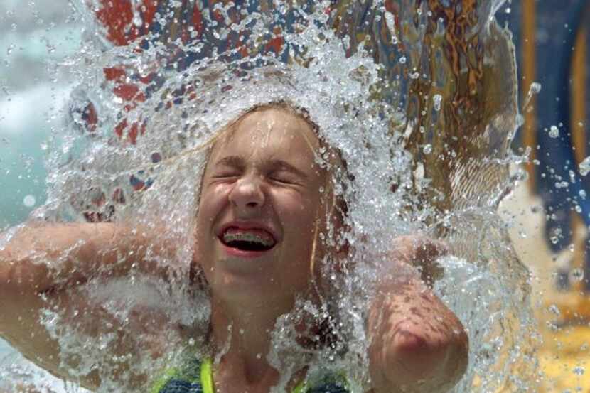 A girl immerses herself under the fountains at City Lake Aquatic Center in Mesquite.