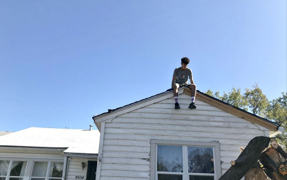 Brandon Avila, a senior at Thomas Jefferson, sat atop the roof of Carlos Rivera's house in Midway Hollow on Tuesday.