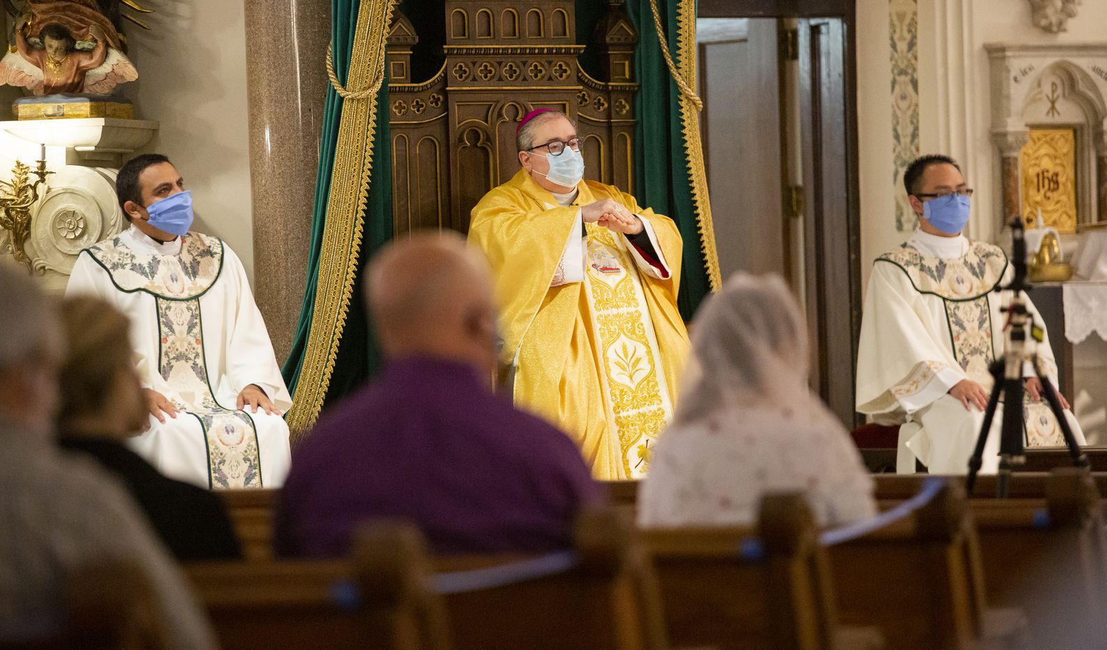 Bishop Michael Olson (center) rubs sanitizer on his hands during mass.