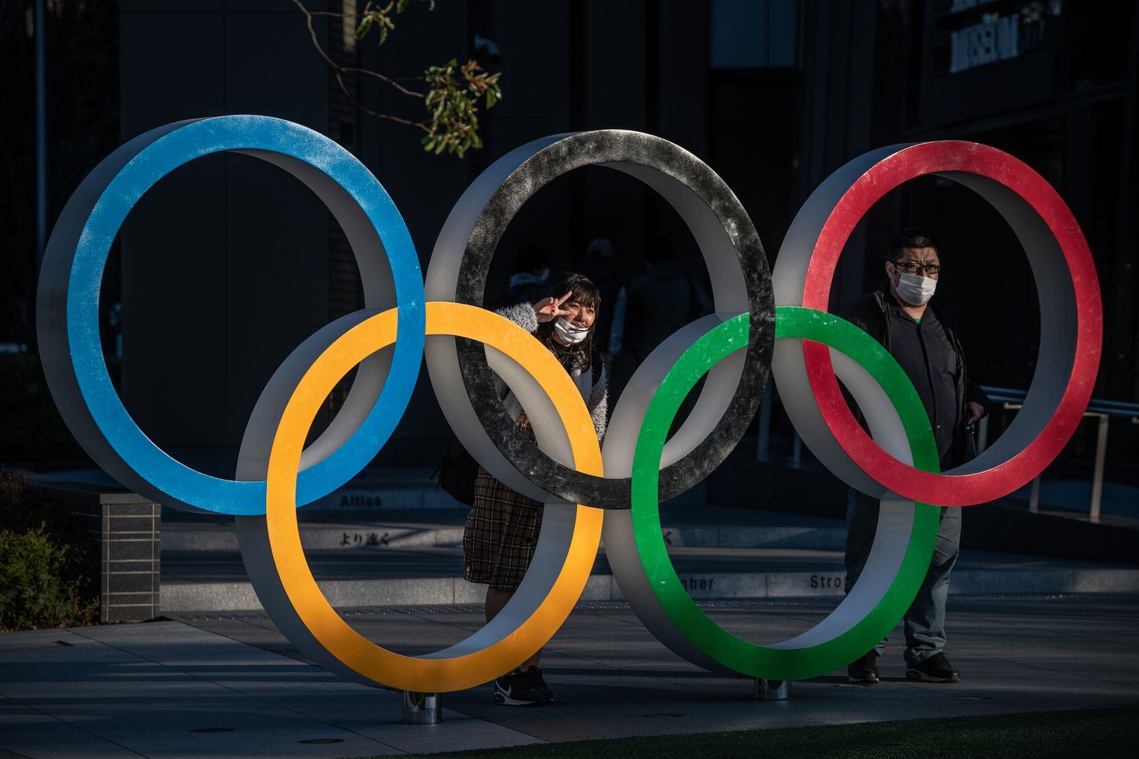People wearing face masks pose for photographs next to Olympic Rings on March 24, 2020 in...
