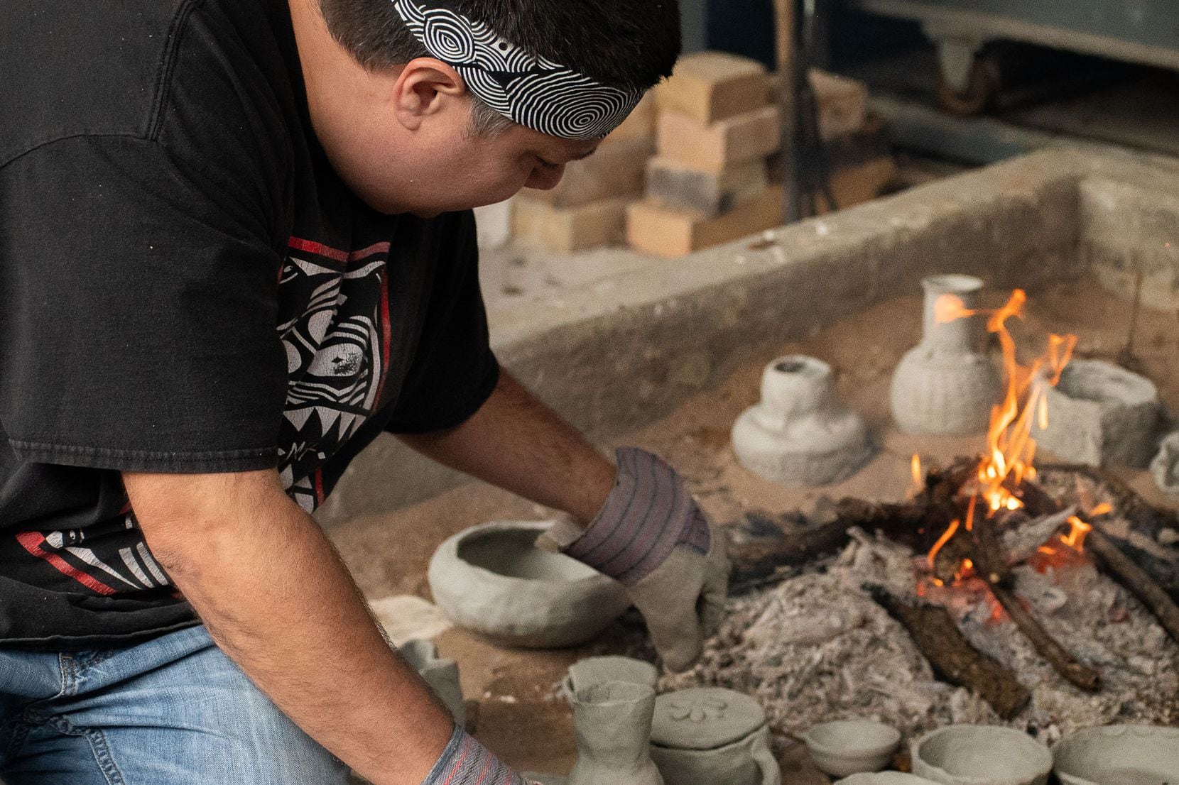 Chase Kahwinhut Earles tends to an open bonfire, which he uses to fire his ceramics, at a...