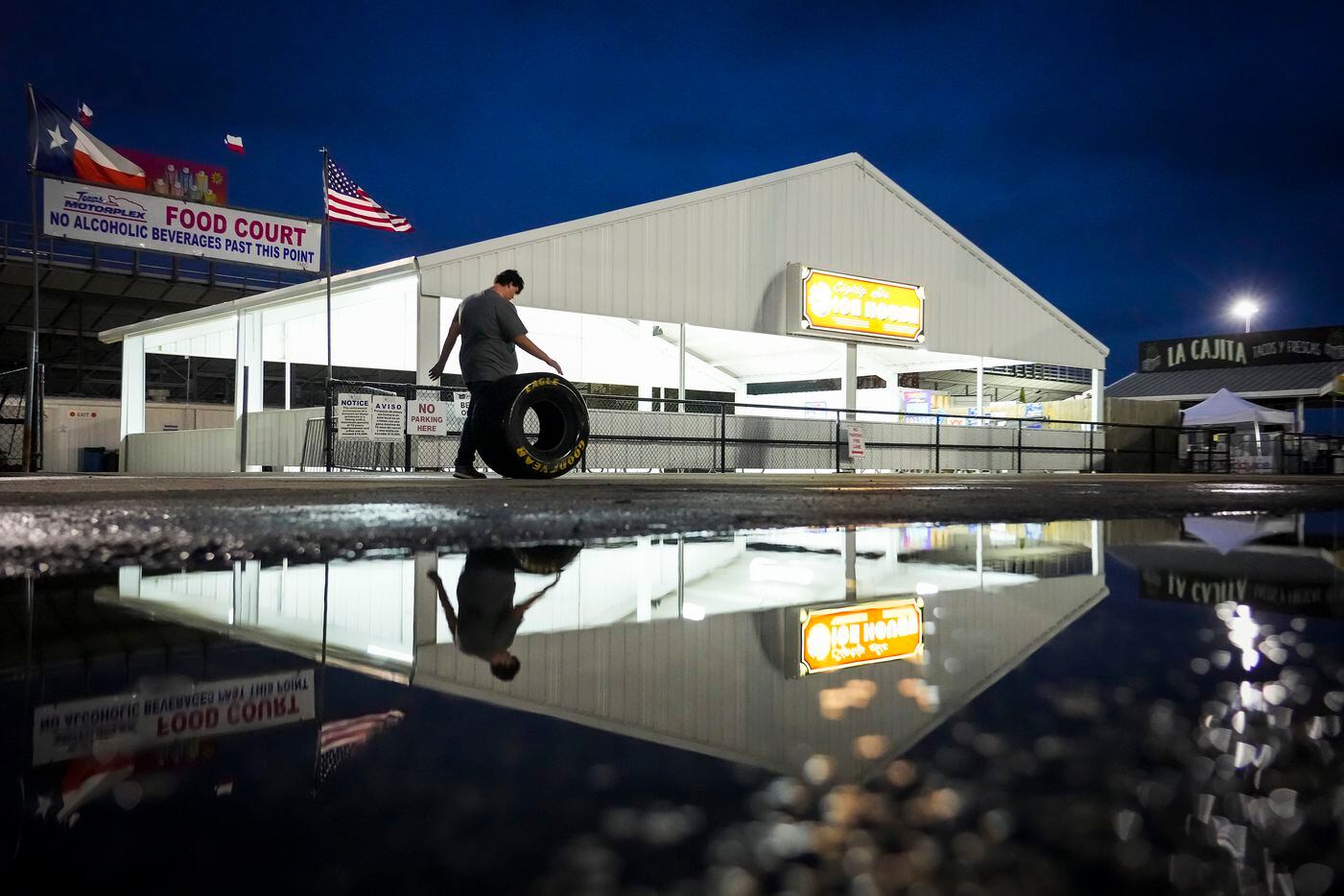 A man rolls a tire past puddles after the the final race of the day at the Texas NHRA...