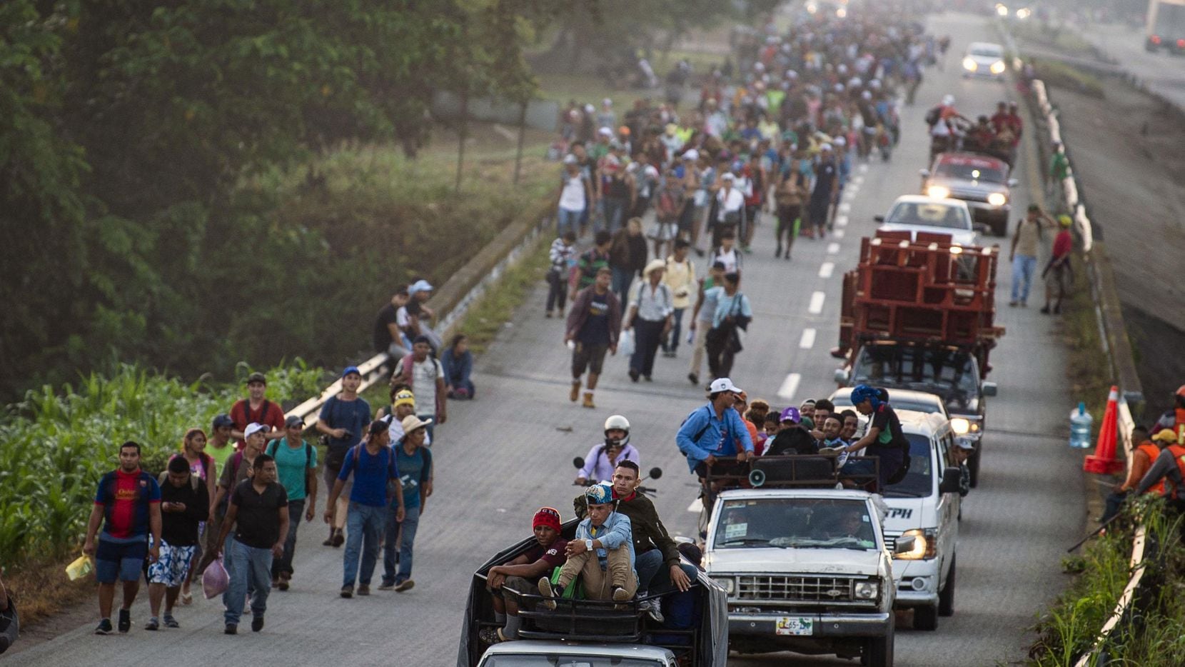 Migrantes hondureños caminan junto a vehículos que transportan a personas desde Chiapas,...